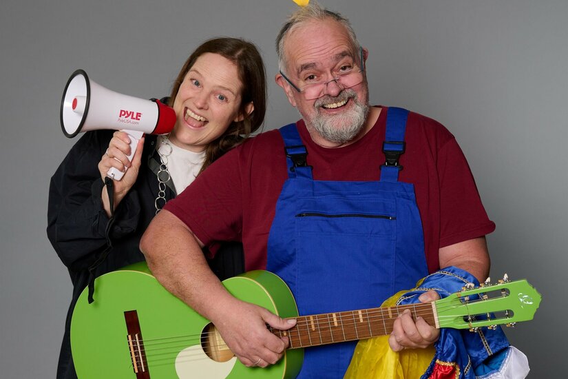 Zwei Personen mit Megafon und grüner Gitarre vor grauem Hintergrund.