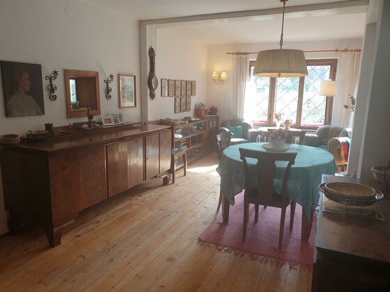 Wohnzimmer und Essbereich Wohn- und Essbereich mit Holzboden, rundem Esstisch, dunklem Sideboard und Wandbildern.