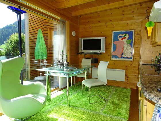 Wohnbereich Golfweg 10 Wohnbereich mit Glastisch, grünen Teppichen und Holzverkleidung.