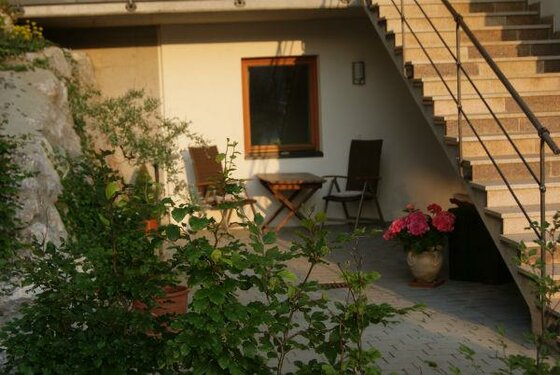 Terrasse Haus Sommer Gepflasterte Terrasse mit Holztisch, zwei Stühlen und einer Außentreppe aus Stein.