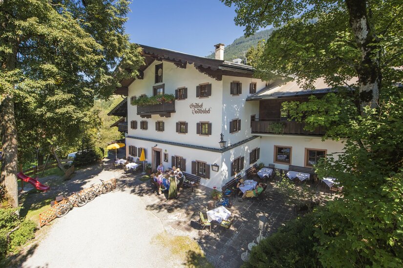 Außenansicht des Gasthofs Jodlbühel mit Sonnenterrasse, Gästen und abgestellten Fahrrädern unter Bäumen.