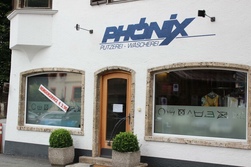 Phönix Ein Geschäft mit dem Namen "Phoenix" für Reinigung und Wäscherei. Die Fassade ist hell und modern mit großen Fenstern.