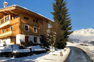 Haus Lazar im Winter Mehrstöckiges Holzhaus in verschneiter Landschaft mit Blick auf ein Gebirgsmassiv unter blauem Himmel.