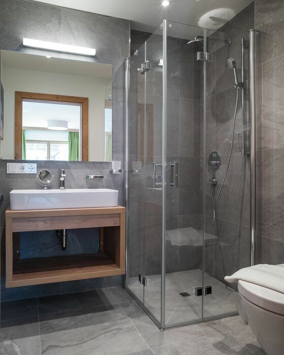 Badezimmer Wagstätt Residenz Jochberg Modernes Badezimmer mit Glasdusche, Waschbecken auf Holzunterschrank und großem Spiegel.