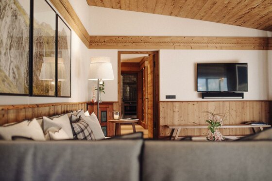 Modernes Wohnzimmer mit Holzdecke, Sofa, Stehlampe und Fernseher an einer hellen Wand.