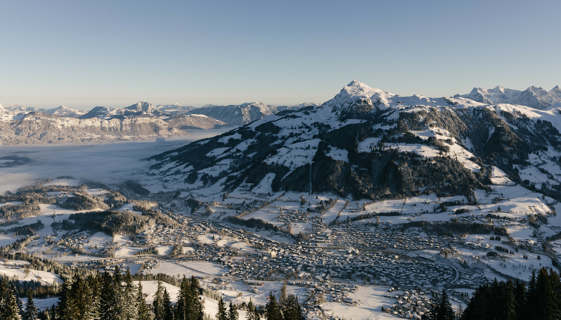 Ein atemberaubender Blick auf schneebedeckte Berge und das Tal, das in sanften Nebel gehüllt ist, unter klarem Himmel.