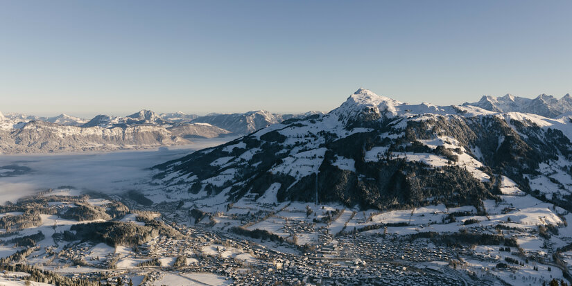 Ein atemberaubender Blick auf schneebedeckte Berge und das Tal, das in sanften Nebel gehüllt ist, unter klarem Himmel.