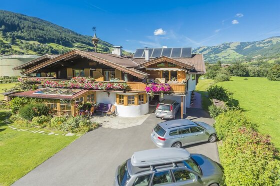 Landhaus Klotz im Sommer Alpines Landhaus mit Blumenschmuck, Parkplatz und Bergpanorama im Hintergrund.