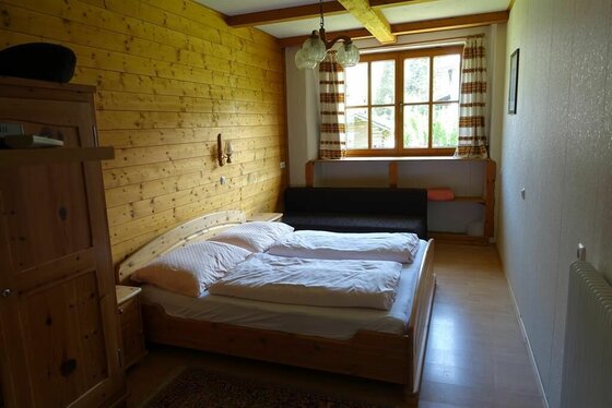 Schlafzimmer im Appartement Neuhaus Schlafzimmer mit Doppelbett aus Holz, holzgetäfelter Wand und Fenster.