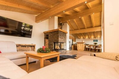 Moderner Wohnbereich mit Holzbalkendecke, Steinkamin, hellem Sofa und Blick auf den Essbereich.