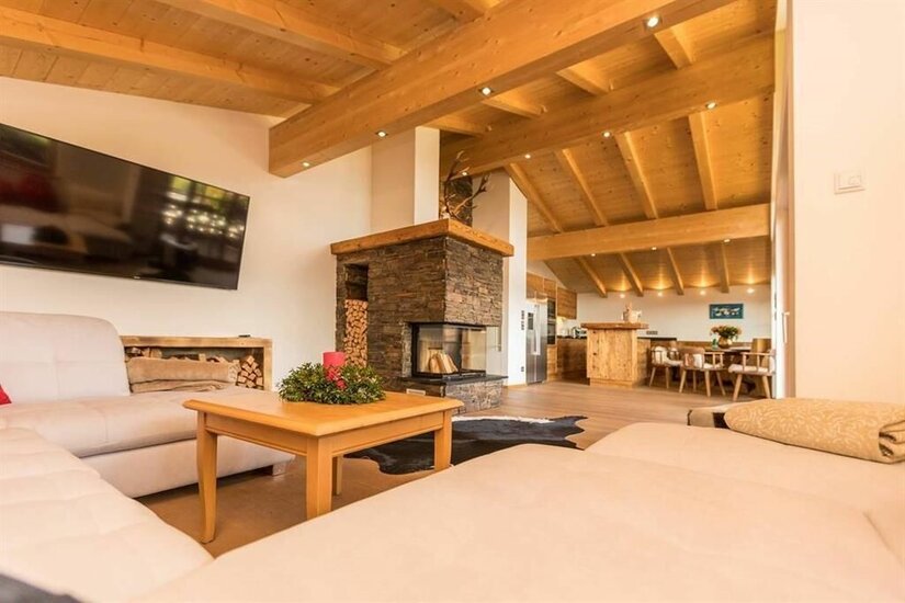 Wohn-Essbereich im Chalet Moderner Wohnbereich mit Holzbalkendecke, Steinkamin, hellem Sofa und Blick auf den Essbereich.