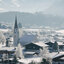 Winterlandschaft in Reith bei Kitzbühel mit Kirche und Häusern, umgeben von verschneiten Bäumen.