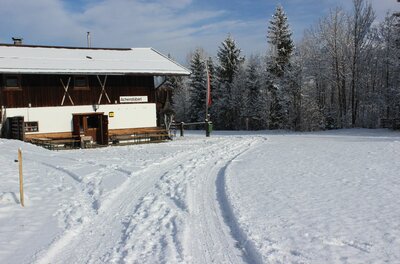 Achenstüberl im Winter Ein verschneites Holzhaus mit weißer Fassade und schneebedecktem Dach neben einer präparierten Winterspur.