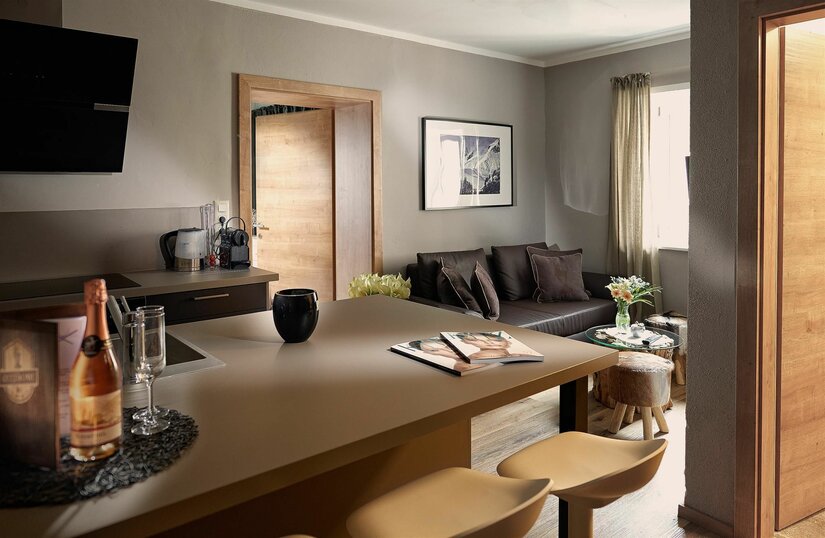 Moderner Wohn- und Essbereich mit Küchentresen, Barhockern und dunklem Sofa.