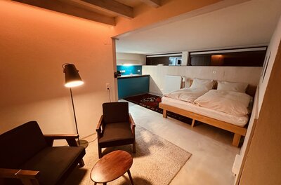 Wohnbereich im Pool House Moderner Wohn- und Schlafbereich mit zwei Sesseln, Holztisch und Doppelbett vor einer Küchenzeile.