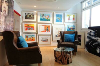 Walentowski Galerie Kitzbühel Ein gemütlicher Raum mit zwei Sessel und einem Couchtisch. Die Wände sind mit bunten Kunstwerken bedeckt.
