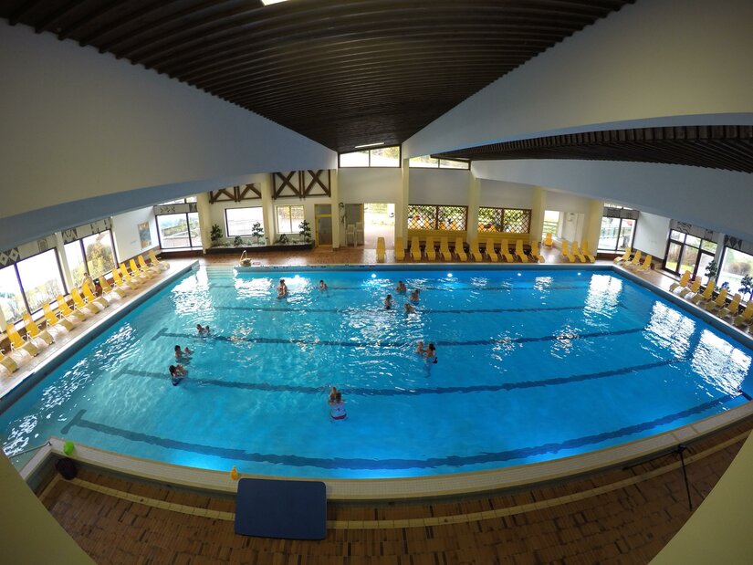 Schwimmbecken Ein Hallenbad mit klarem Wasser und mehreren Schwimmern. Rund um das Becken stehen gelbe Liegen.