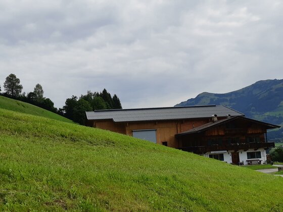 Ferienwohnung Schatzhof Ein traditionelles Holzhaus mit angebautem Stallgebäude an einem grünen Grashang vor bewaldeten Bergen.
