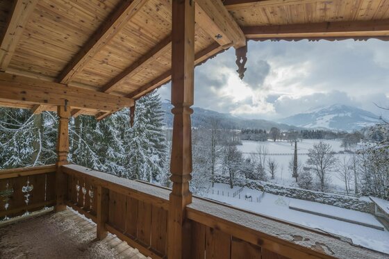 Winterlicher Ausblick vom Balkon Blick von einem hölzernen Balkon auf eine verschneite Tallandschaft mit Bergen unter bewölktem Himmel.