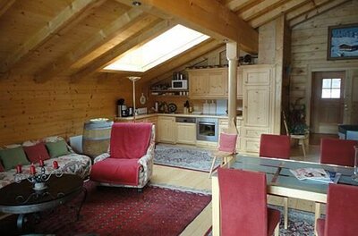 Wohnbereich Appartment Ölberg Wohn- und Essbereich in einer Holzhütte mit Dachschräge, Küchenzeile und roten Polstermöbeln.