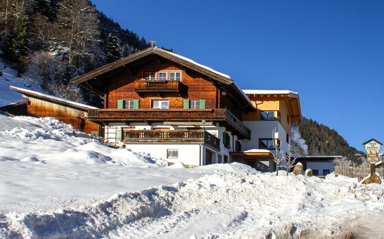 Ferienhof Oberstaudach Winter Alpiner Ferienhof mit Holzfassade und Balkonen in einer verschneiten Winterlandschaft unter blauem Himmel.