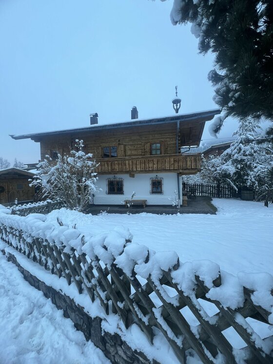 Ein charmantes Holzhaus im Schnee, umgeben von einem gepflegten Garten. Die Landschaft ist winterlich und friedlich.