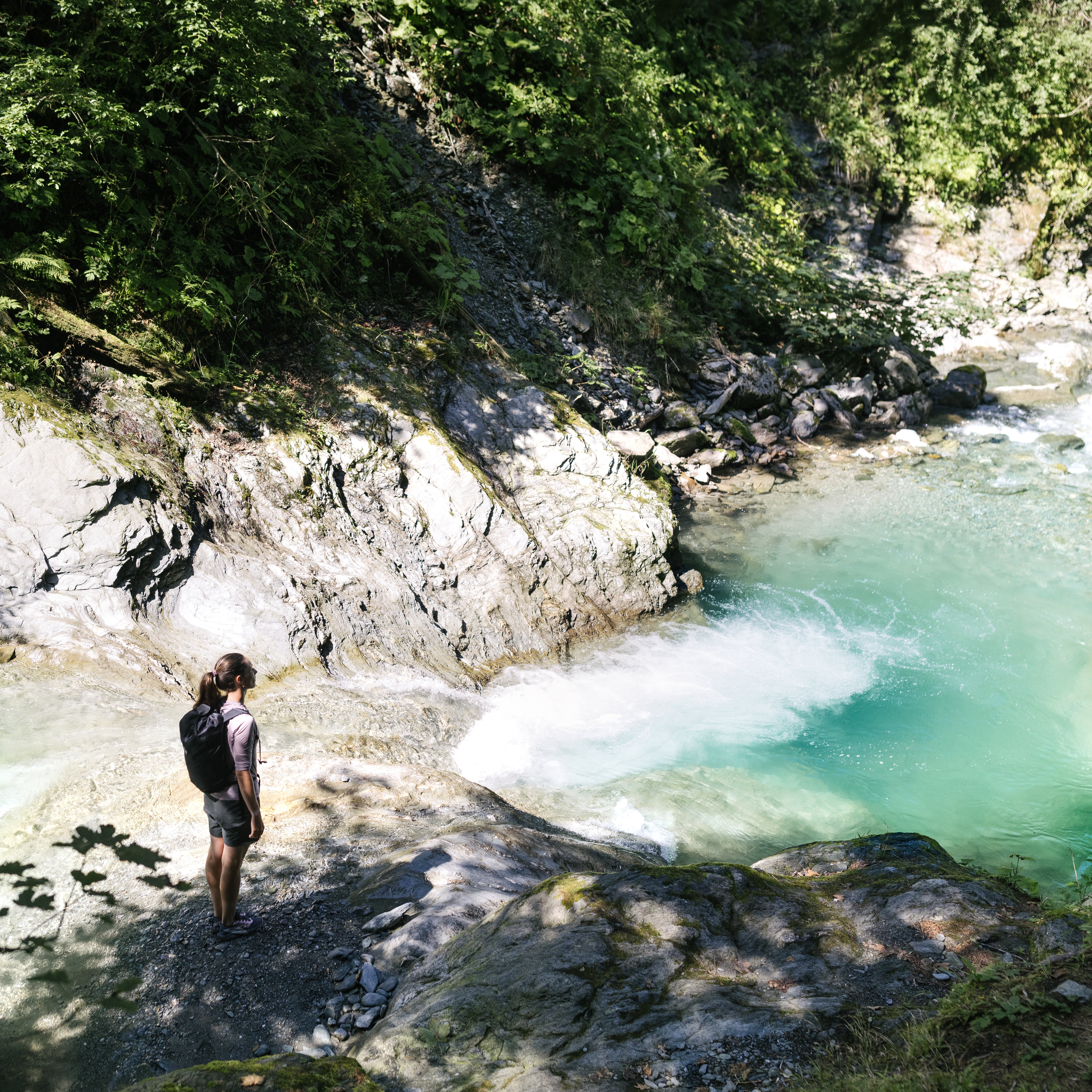 A woman is standing on a rock, looking down at the turquoise-green water below