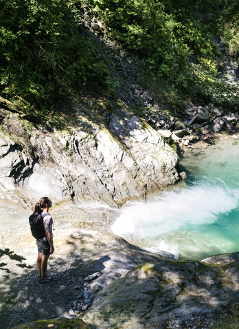 A woman is standing on a rock, looking down at the turquoise-green water below