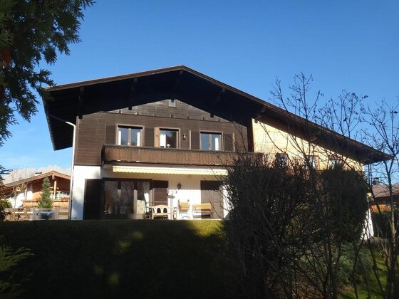 Außenansicht Apartment Panorama Zweistöckiges Gebäude mit dunkler Holzfassade, Balkon und Terrasse vor blauem Himmel.