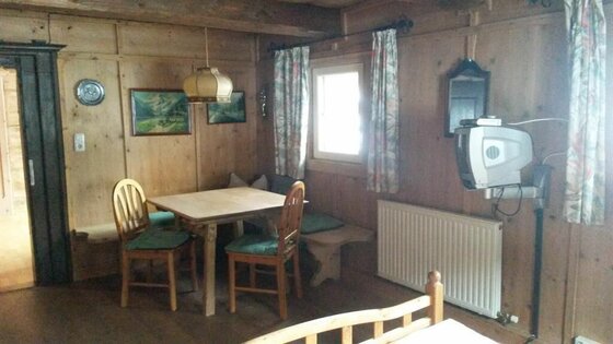 Rustikale Sitzecke aus Holz mit Tisch, zwei Stühlen, Eckbank und einem kleinen Fernseher an der Wand.