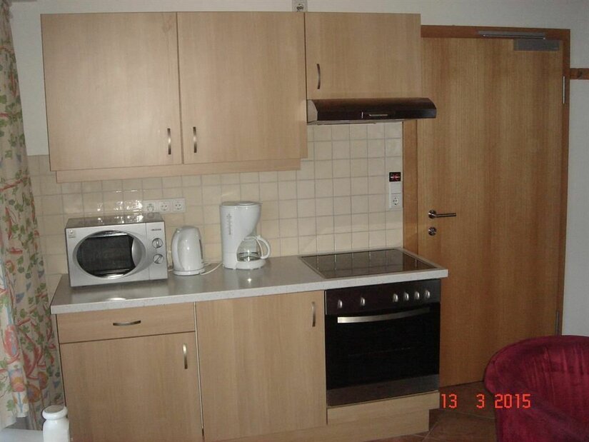 Küchenzeile im Appartement Neuhaus Kleine Küchenzeile aus hellem Holz mit Herd, Backofen, Mikrowelle und Kaffeemaschine.