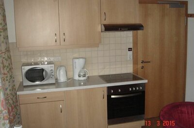 Küchenzeile im Appartement Neuhaus Kleine Küchenzeile aus hellem Holz mit Herd, Backofen, Mikrowelle und Kaffeemaschine.