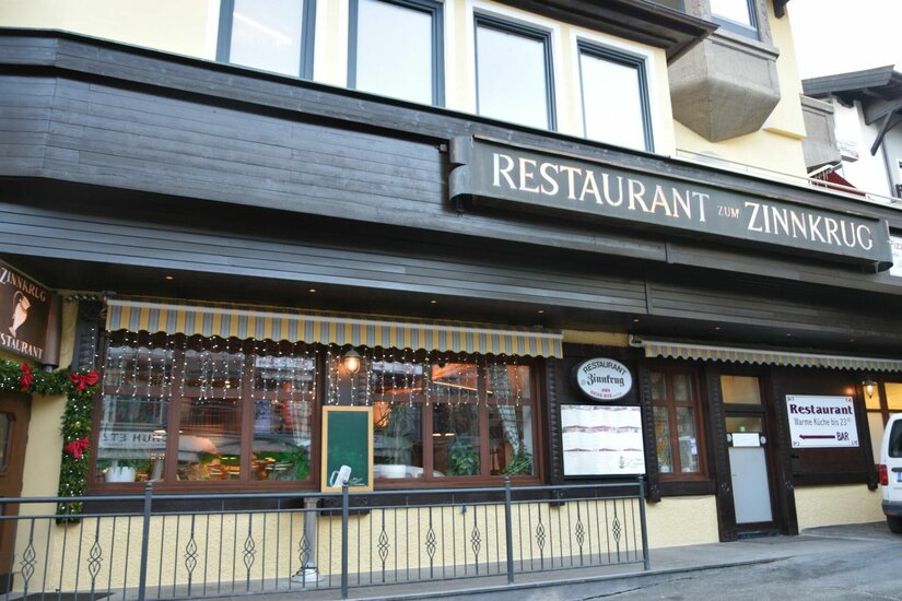 Außenansicht des Restaurants Zum Zinnkrug mit dunkler Holzfassade und beleuchteten Fenstern.