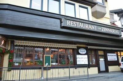 Restaurant Zum Zinnkrug Außenansicht des Restaurants Zum Zinnkrug mit dunkler Holzfassade und beleuchteten Fenstern.