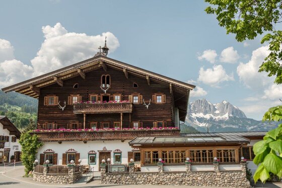 Landgasthof Reitherwirt Traditionelles Holzgebäude mit Blumenbalkonen vor schneebedeckten Berggipfeln.