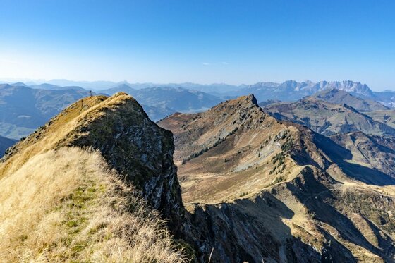 Blick vom Bischof Blick auf einen schmalen Graskamm und felsige Berggipfel unter blauem Himmel.