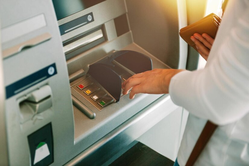 Nahaufnahme einer Person, die eine PIN an einem Bankautomaten eingibt.