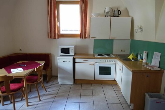 Küchenzeile im Appartement Neuhaus Kleine Einbauküche mit weißer Front, Elektroherd und angrenzender Sitzecke mit Holztisch.