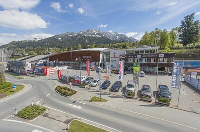 Sportpark Kitzbühel Außenansicht des Sportparks Kitzbühel mit Parkplatz, Gebäudekomplex und Bergen im Hintergrund.