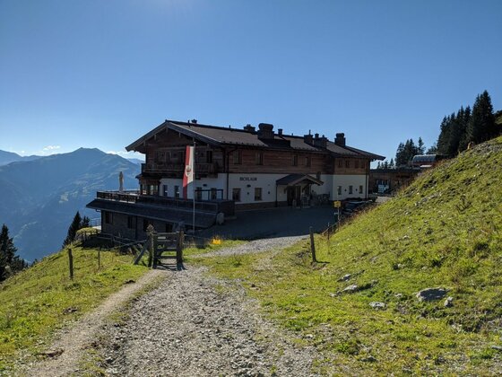 Berggasthaus Bichlalm Großes Berggasthaus aus Holz und Stein an einem Schotterweg vor Gebirgspanorama.