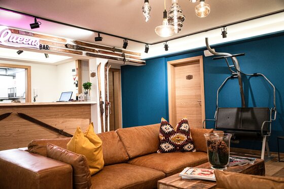 Loungebereich mit braunem Ledersofa, Holztisch und einem umgebauten Sessellift als Sitzgelegenheit vor blauer Wand.