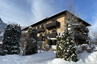 Das EDELWEISS KITZBÜHEL im Winter Mehrstöckiges Hotelgebäude mit Holzbalkonen in einer verschneiten Winterlandschaft unter blauem Himmel.