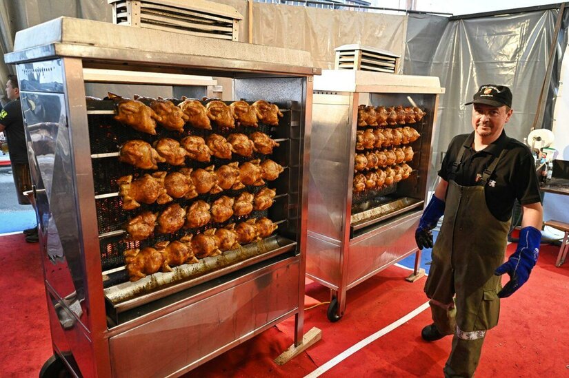 Hähnchengrill beim Feuerwehrfest Ein Mann in Arbeitskleidung steht neben zwei großen Grillstationen mit zahlreichen Brathähnchen am Spieß.