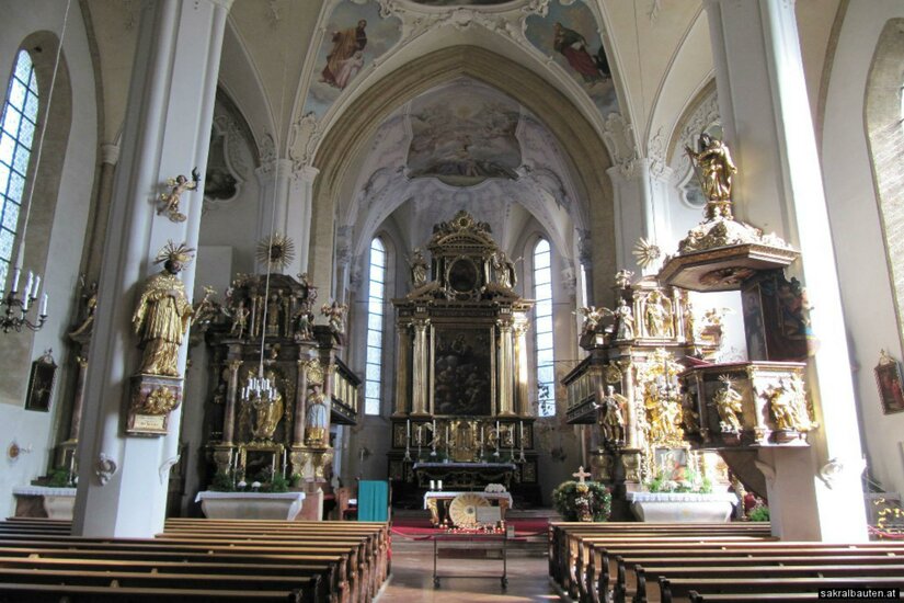 Stadtpfarrkirche Ein schöner Kircheninnenraum mit kunstvollen Altären und einer hohen Decke. Die Bänke sind aufgereiht und der Altarbereich ist zentral sichtbar.