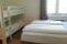 Ein einfaches Zimmer mit zwei Einzelbetten und einem Etagenbett. Es hat große Fenster und hellen Holzfußboden.