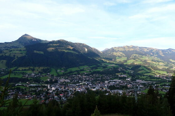 Blick auf Kitzbühel Blick von oben auf eine Ortschaft im Tal vor bewaldeten Bergen und grünen Hängen unter blauem Himmel.