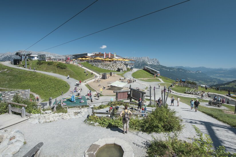 Ein malerischer Bergort mit vielen Besuchern und klar blauem Himmel. Die Umgebung ist grün und einladend, ideal für Outdoor-Aktivitäten.