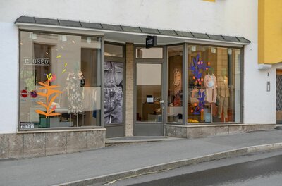 Closed Store Kitzbühel Schaufensterfront eines Bekleidungsgeschäfts mit Mannequins und farbigen Grafiken an der Glasfläche.