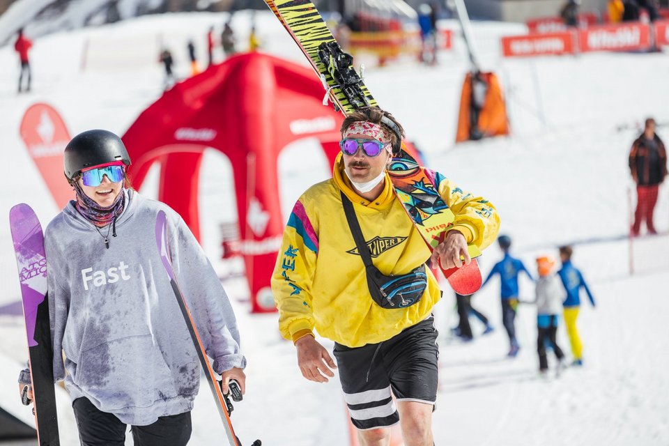 A couple in colorful outfits walks down the ski slope