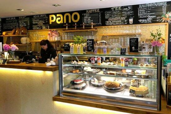 Pano Brot und Kaffee Verkaufstheke eines Cafés mit Kuchentheke aus Glas und einer großen Menütafel im Hintergrund.